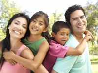 Young family with two kids smiling by trees 