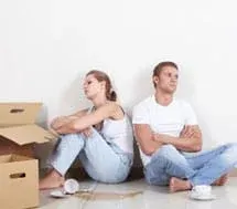 Man and woman sitting back to back with arms crossed next to boxes