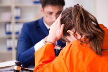 Woman in handcuffs with her head in hands sitting accross from a lawyer