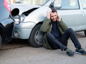 Man resting against his crashed car while making a phone call