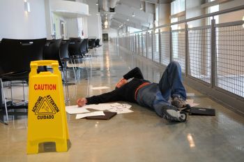 Man on the floor with his hand on his face near a wet floor sign