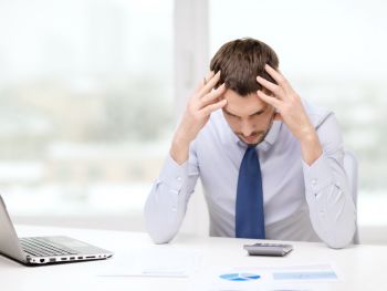 Stressed out man holding head in front of calculator and laptop