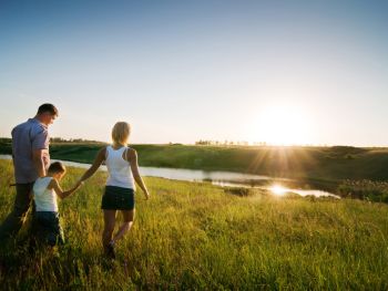 Two parents holding their child's hand in a field at sunset