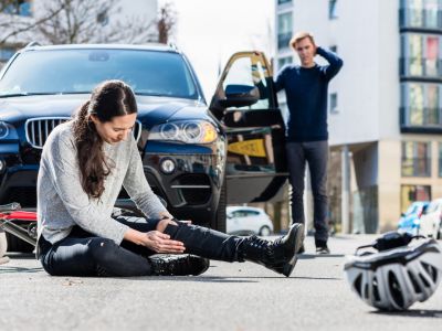 Sitting woman holding her knee next to a bike and helmet and a man with his arm on his head standing on the driver's side of a car