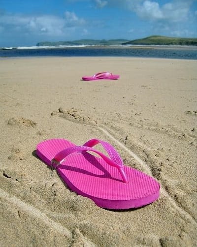 pink flip flops spread out in sand on a beach