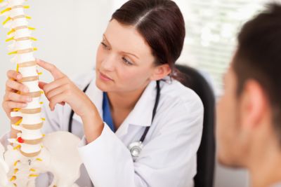 Female doctor with patient pointing to an area on a plastic spine visual aid