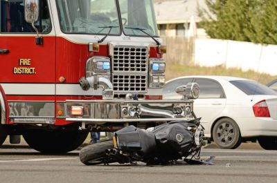 Damaged motorcycle laying on the road and a firetruck close behind it