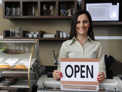 Woman standing behind counter holding an open sign