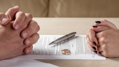 Close up of a man and woman's hands folded on either side of a document with a pen and rings sitting on top