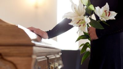 Person with flowers and hand on a casket 