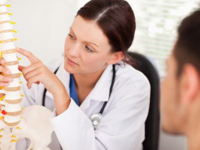 Woman in white coat with stethoscope around her neck pointing at a model of the spine