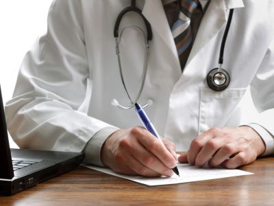 Man in white coat with stethoscope around his neck taking notes