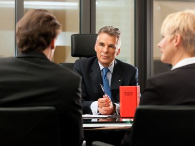 Man in suit holding a pen sitting across from a man and woman at a table