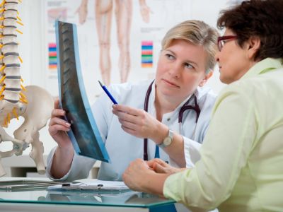 Woman in white coat with stethoscope around her neck sitting with another woman pointing with a pen at imaging