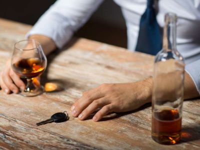 Man drinking an alcoholic beverage with an almost empty bottle on the table reaching for his car keys