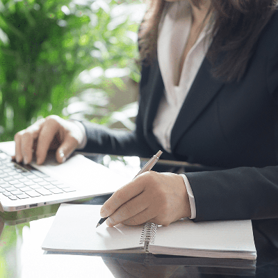Woman working at a computer and writing in notebook