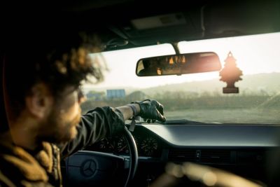 Man sitting in the drivers seat with his arm stretched over the steering wheel of a car