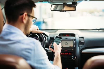 Man sitting in drivers seat with hand on the wheel looking down at his phone