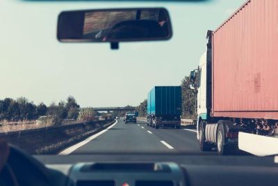 View from inside a car on a road with two semi trucks on the right 