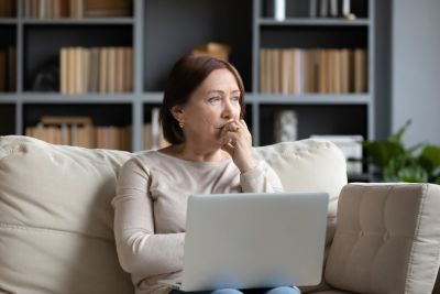 Older woman sitting with computer on her lap and hand to her face looking away