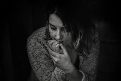 Woman in long sleeved top hunched over biting her nails