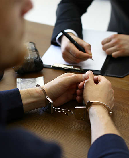 Police Officer Interrogating Criminal in Handcuffs at Desk Indoors