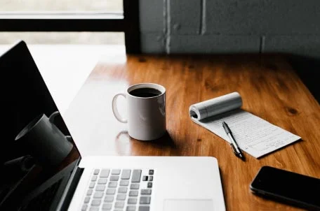 Open laptop, coffee mug, notepad, and phone on table