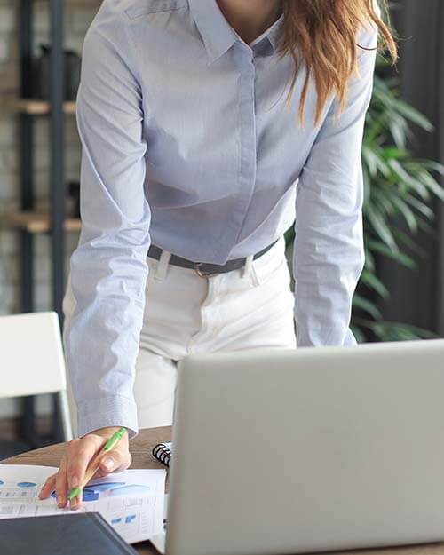 A woman working at her desk, pen in hand, in front of her laptop