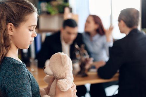 young girl holding a teddy bear with parents fighting in the background