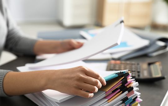 Person sitting at desk with stacks of paperwork