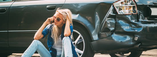 Person sitting by wrecked car talking on the phone