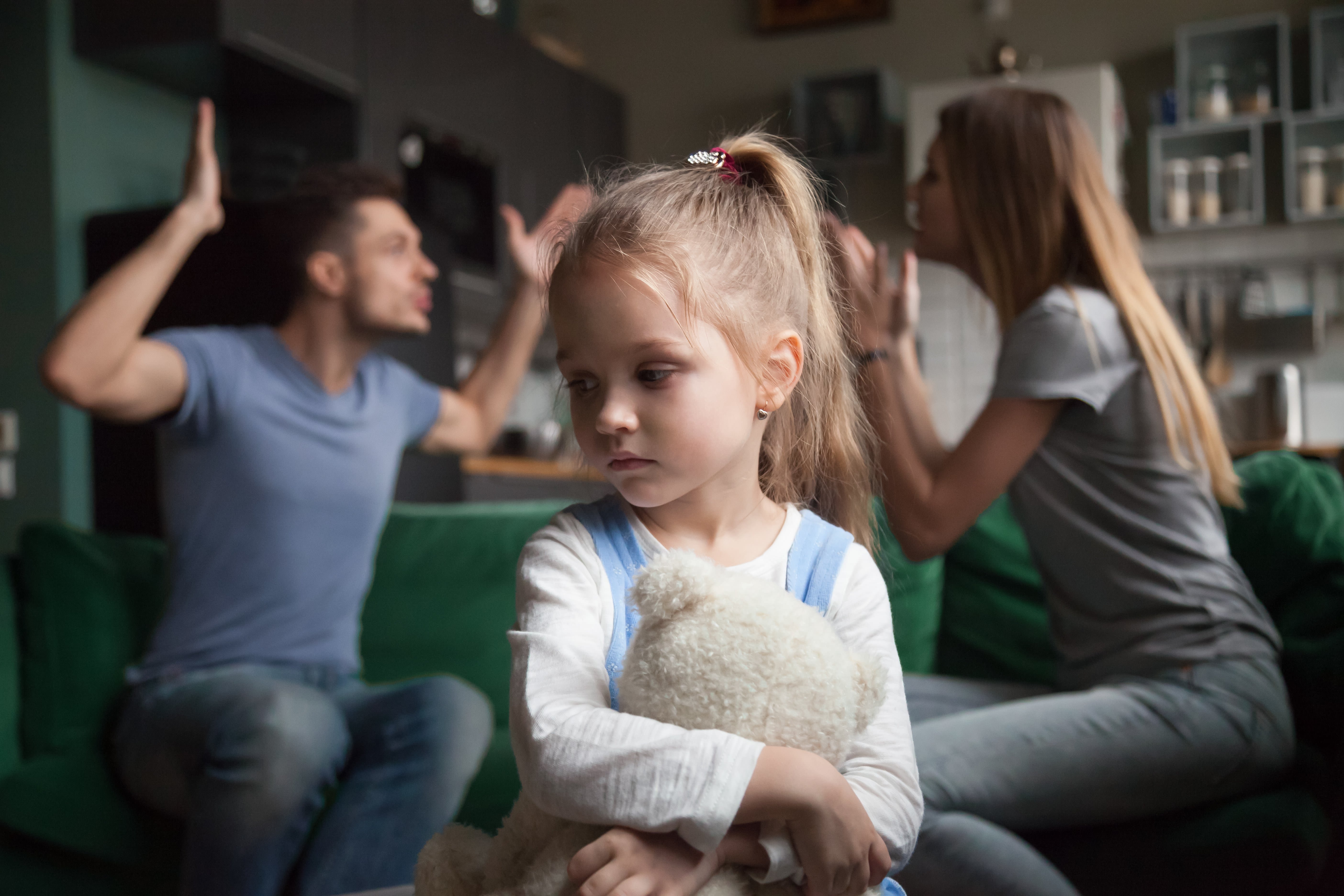 A little girl looking upset while two adults argue in the background