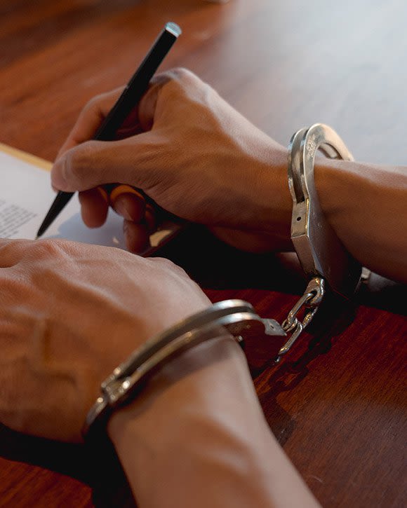 Close up of hands in handcuffs signing paperwork