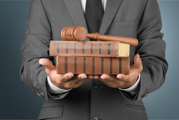 Man in gray suit holding books and gavel