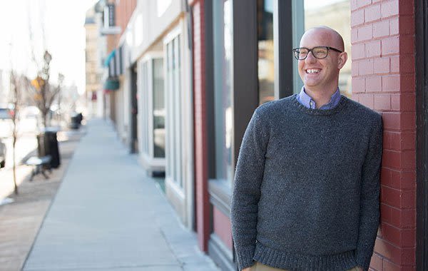 Attorney Paul Benson Leaning Against the Red Brick Wall in a Relaxed Posture