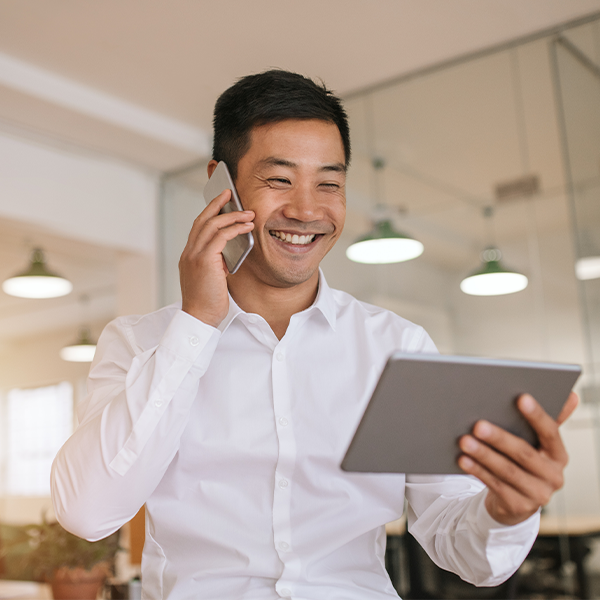 Person holding phone to ear while smiling at tablet in hand