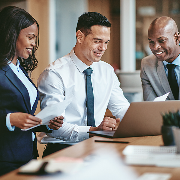 Three people in business wear looking at computer at desk