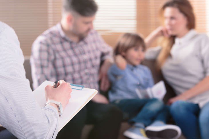 Mom, dad, and son sitting on couch while another man writes on clipboard