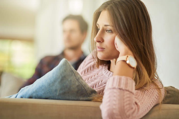 Upset woman on couch leaning on hand with man in background