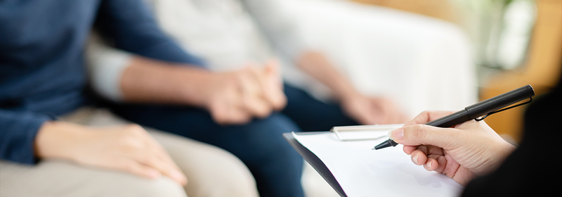 Person writing on clipboard with two people holding hands