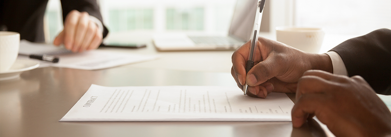 Two people in suits sitting at desk signing paperwork