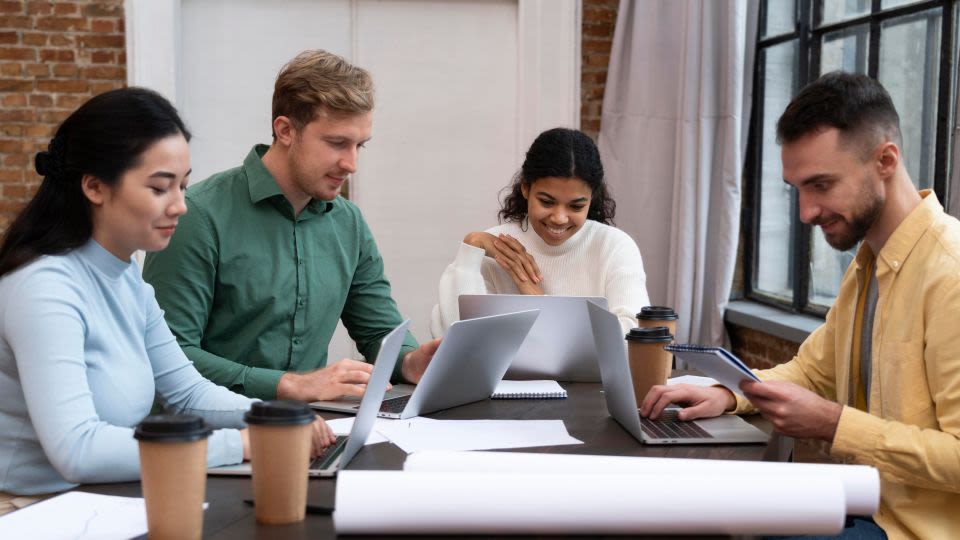 Four colleagues sit around a table while using laptops.