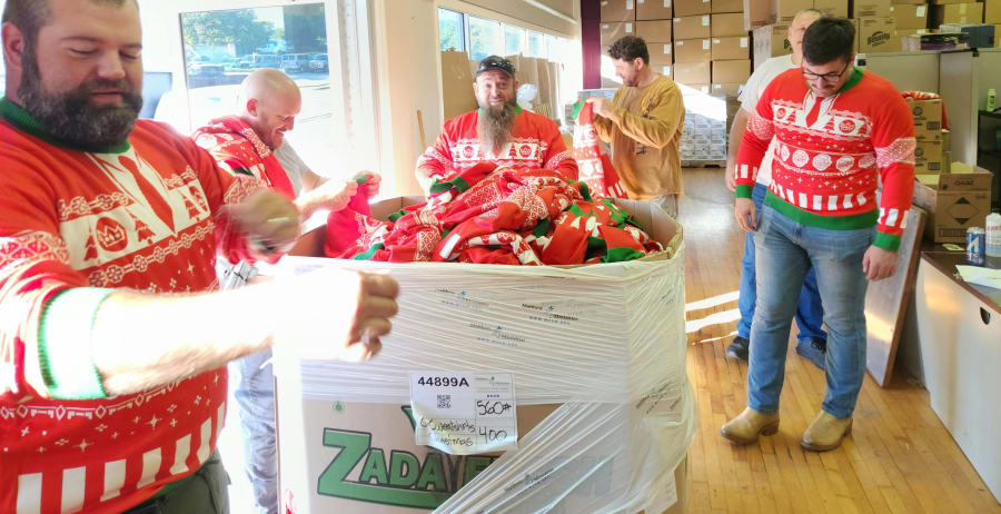 Group of volunteers in matching ugly Christmas sweaters gathered around a pallet of wrapped holiday gifts