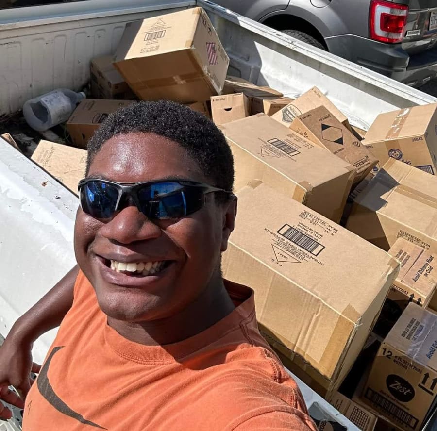 Volunteer smiling for a selfie in the back of a pickup truck loaded floor to ceiling with donation boxes