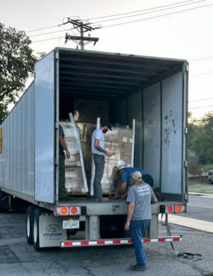 Three volunteers working inside the back of a tractor-trailer, organizing pallets of donated supplies