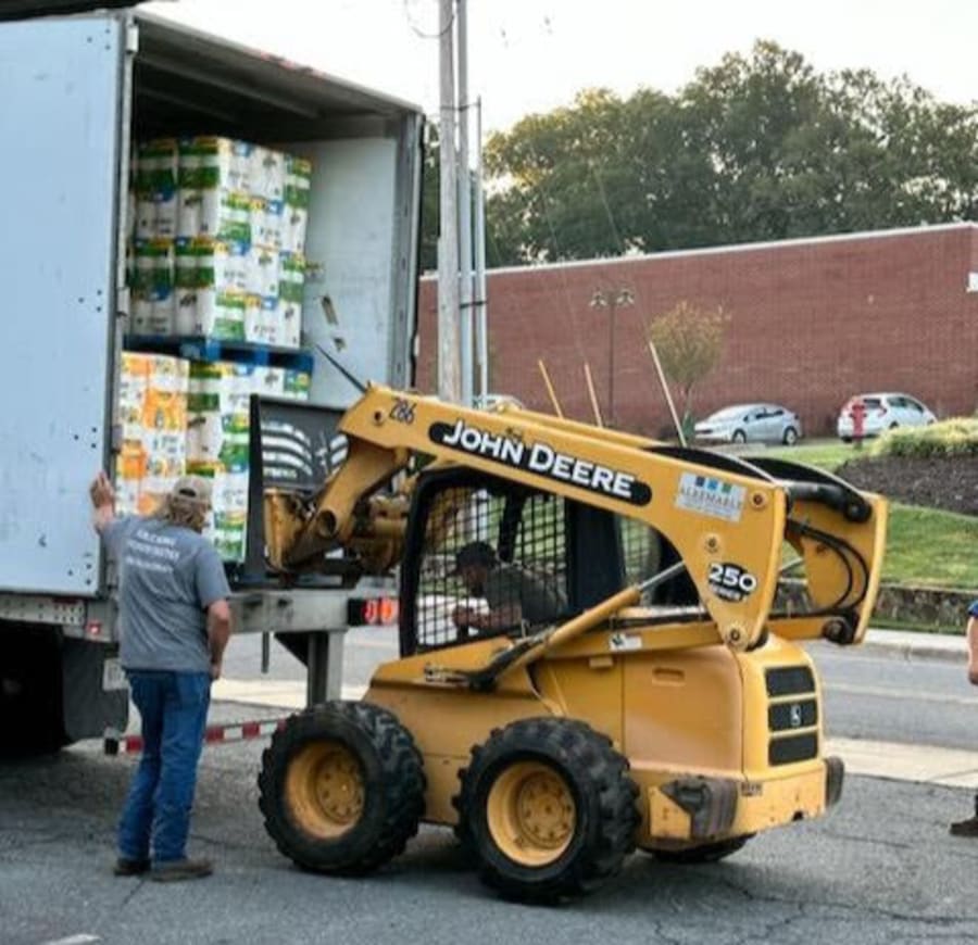 John Deere skid-steer loading pallets of paper goods into the back of a tractor-trailer