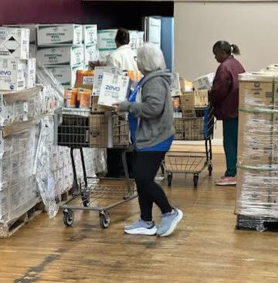 Volunteers pushing shopping carts loaded with cleaning supplies and household goods across the warehouse floor