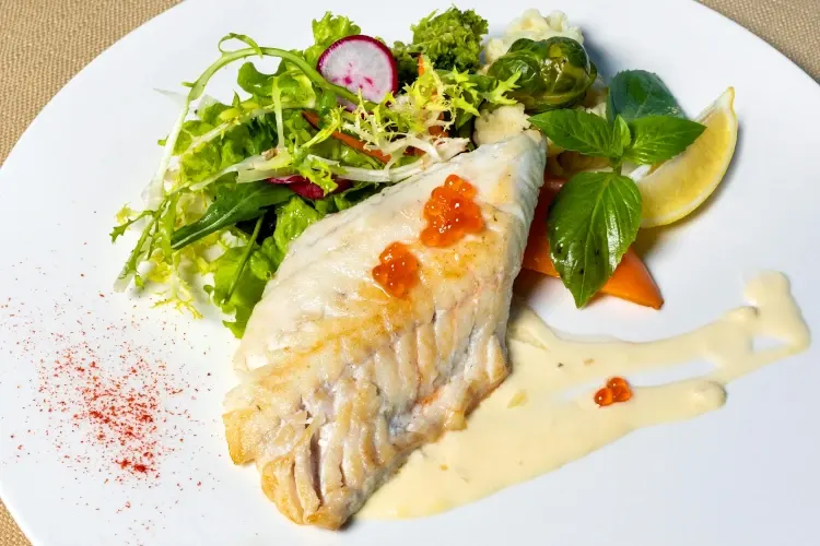 Grilled cod with white sauce and garnish on a plate