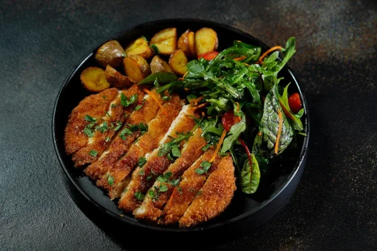 Pork schnitzel with garnish and potatoes in a black bowl