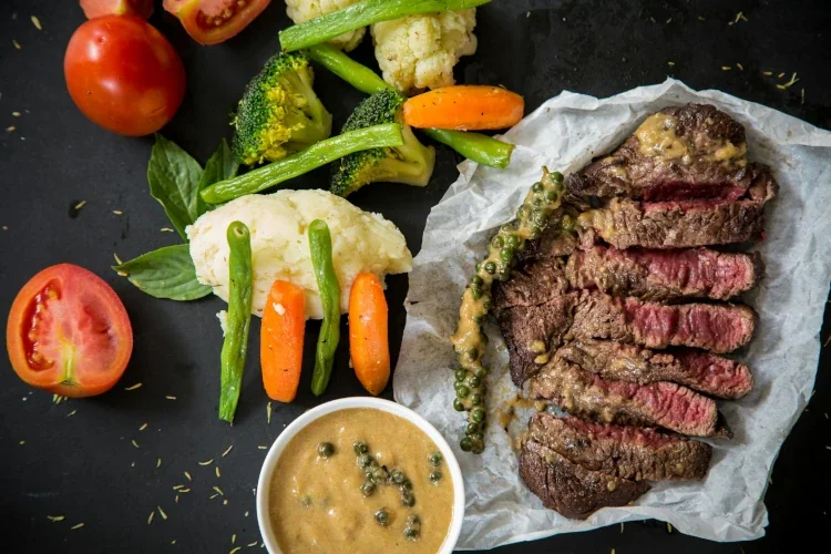 A cut steak next to vegetable side dishes.